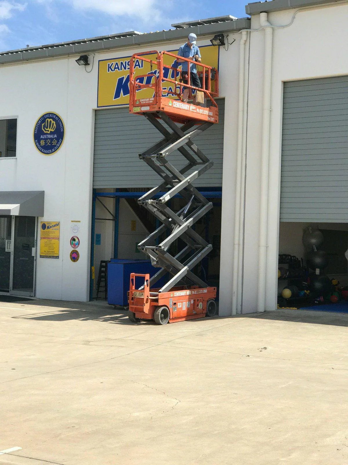 Electrician working from an orange scissor lift above the roller door of a commercial unit