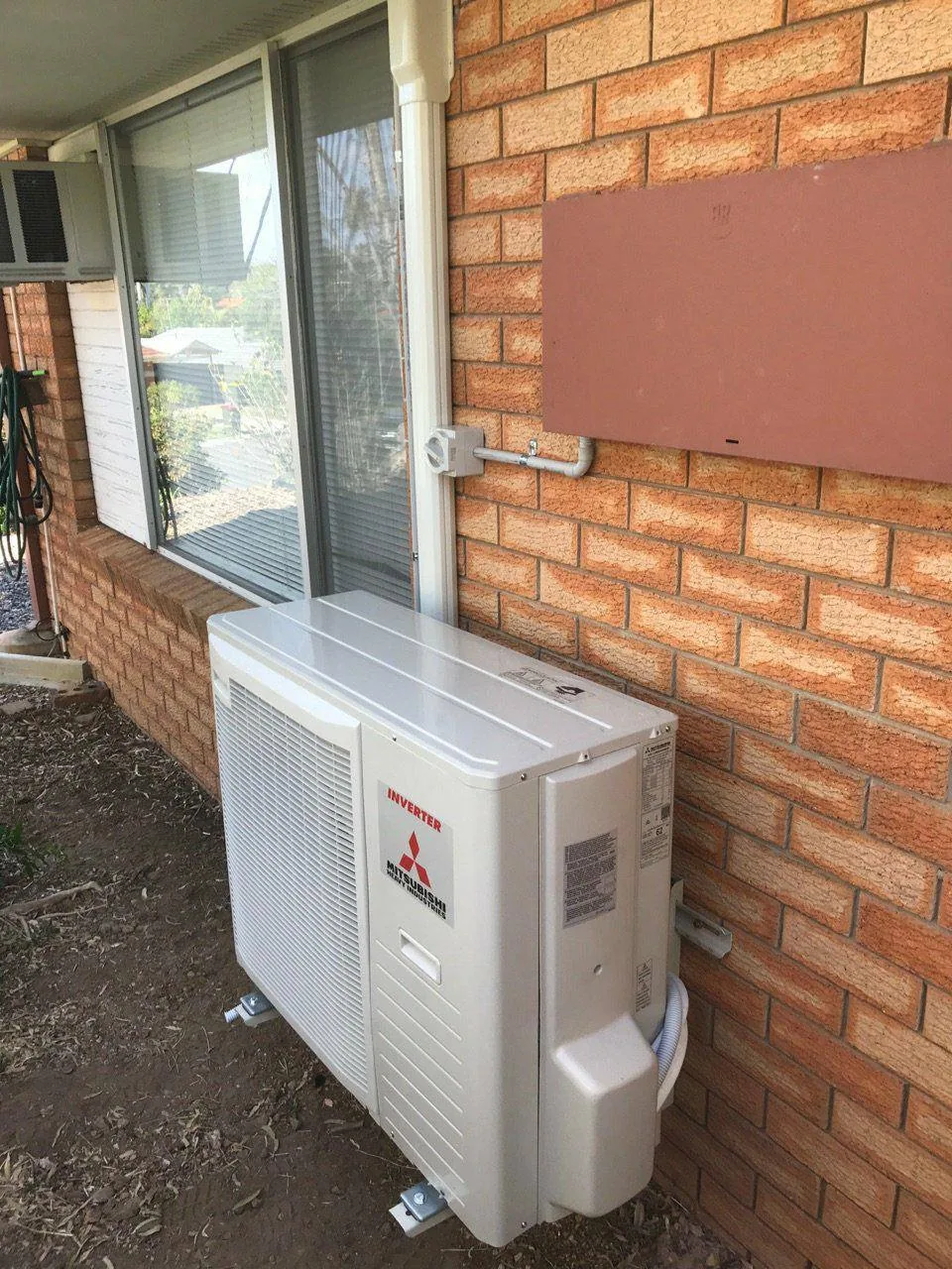 Inverter air conditioner outdoor unit installed beside a window on a brick house