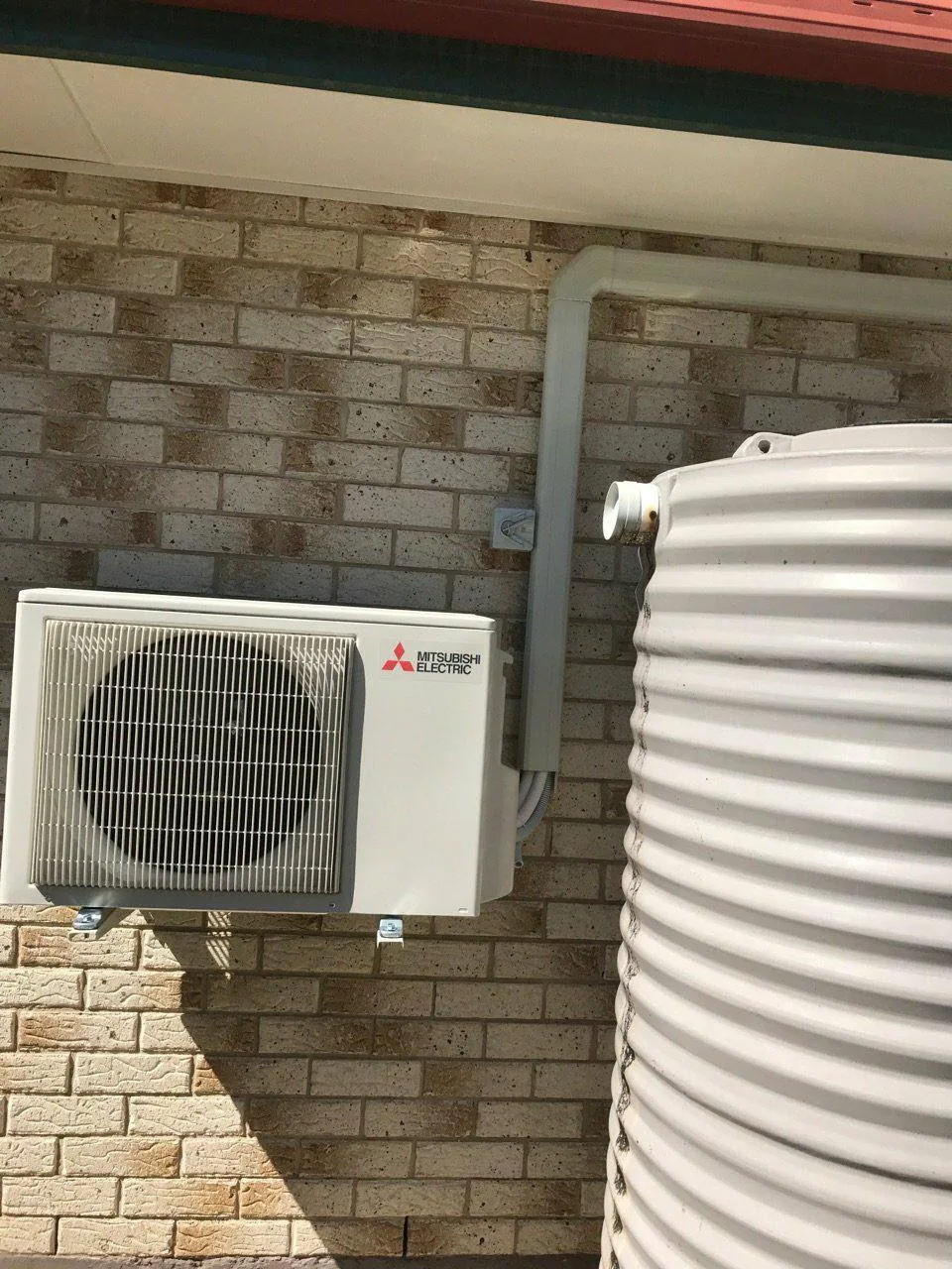 Mitsubishi Electric outdoor unit on a brick wall next to a round rainwater tank