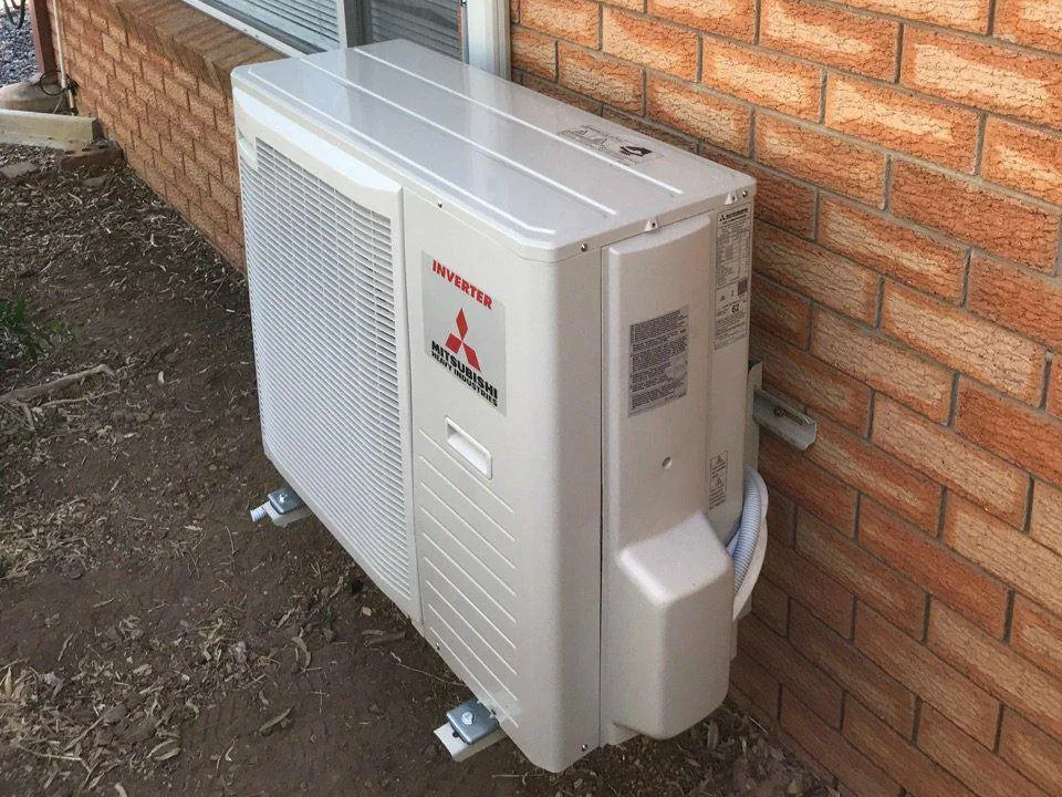Mitsubishi inverter air conditioner outdoor unit installed on brackets against a brick house