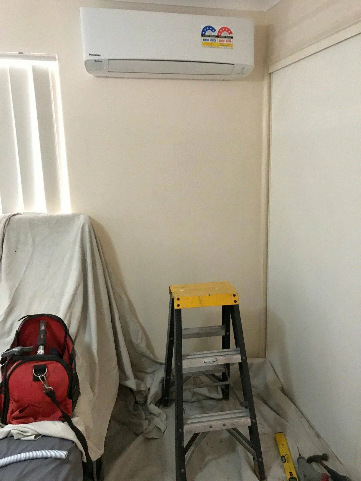 Panasonic split system indoor unit newly mounted high on a bedroom wall, drop sheets protecting the furniture